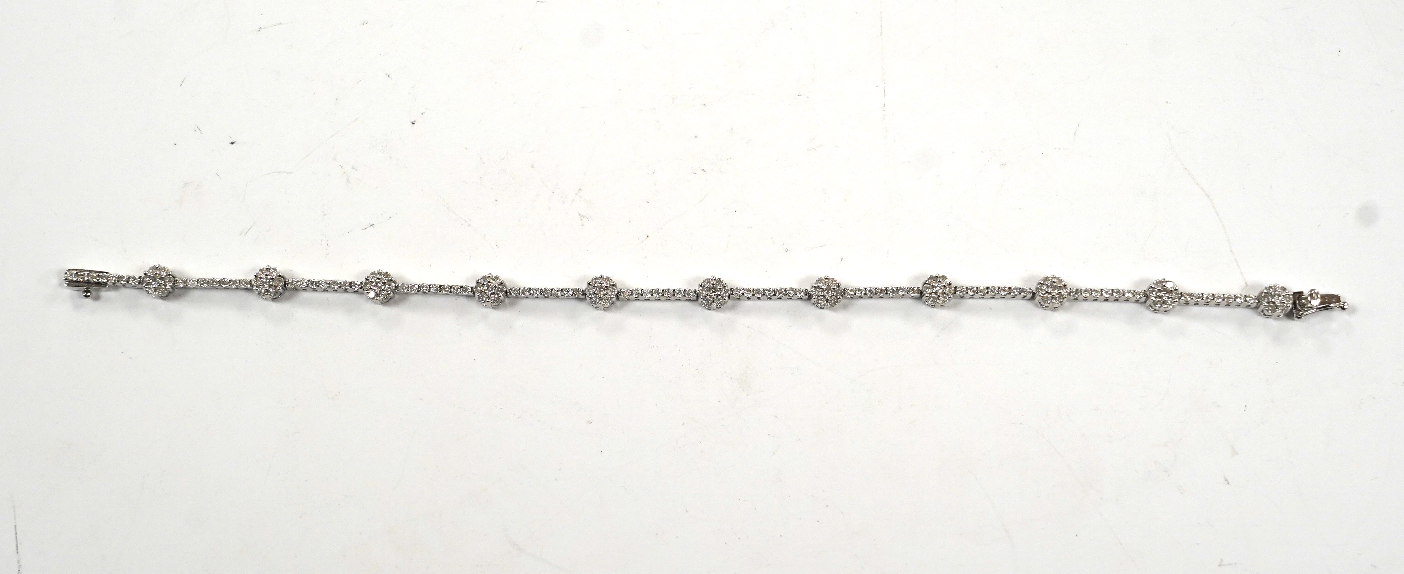 A modern 18k white metal and diamond cluster set line bracelet, 17.8cm, gross weight 8.8 grams.